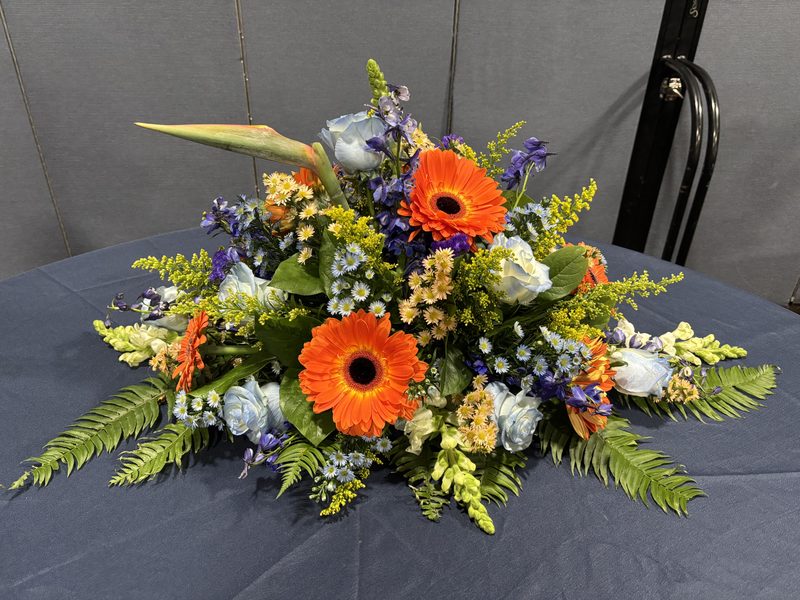 Graveside Spray - Vibrant orange gerbera daisies with blue and gold accents
